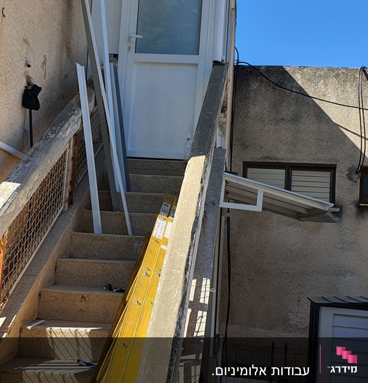 פרופילי אלומיניום מונחים על מדרגות ליד דלת לבנה